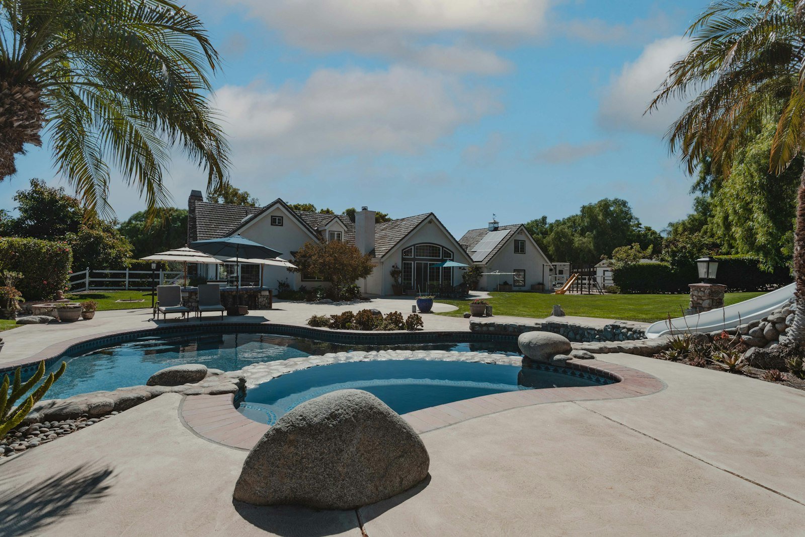 A backyard pool surrounded by palm trees, boulders and tropical landscaping